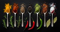 Colorful spices and herbs arranged in wooden spoons on dark background. Culinary ingredients including turmeric, paprika, pepper, salt for cooking and seasoning.