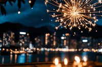 Glowing sparkler against blurred city skyline at night with bokeh lights reflecting on water surface and festive candles in foreground creating magical atmosphere.