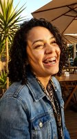 Happy young mixed-race woman with braces smiling at outdoor cafe terrace during golden hour sunset wearing denim jacket for lifestyle content.