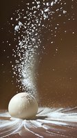 White sphere with explosive powder burst against dark brown background, creating dynamic motion effect with scattered particles and dramatic lighting.