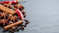 Aromatic winter spices including cinnamon sticks, star anise, cloves and chili peppers arranged on dark slate surface for seasonal cooking and baking recipes.