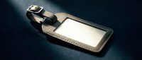 Leather luggage tag with blank white label and metal clasp on dark surface for travel identification and baggage organization purposes.