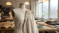 Linen garment on dressmaker mannequin in bright fashion design studio workspace with fabric samples and sewing materials for clothing production.