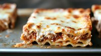 Classic meat lasagna with layers of pasta, ground beef, tomato sauce and melted mozzarella cheese shown in cross section on dark baking sheet, close up view.