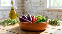 Fresh colorful chili peppers in wooden bowl with olive oil and herbs on rustic kitchen counter for cooking and culinary preparation.