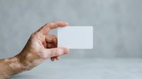 Senior male hand holding blank white business card against neutral gray background for corporate branding and professional networking purposes.