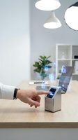 Hand reaching toward futuristic biometric scanner device with holographic security icons in modern office workspace for digital authentication technology.