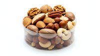 Mixed nuts and dried fruits in glass bowl isolated on white background for healthy snacking and cooking recipes.