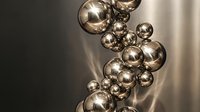 Modern metallic spheres floating in warm light creating elegant shadows and reflections for luxury design concepts and contemporary decor.