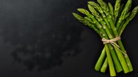 Fresh green asparagus bunch tied with twine on dark background, minimalist food photography composition with copy space for menu design.