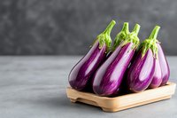 Fresh purple eggplants with green stems arranged on wooden serving board against gray background, raw organic produce for healthy cooking and Mediterranean cuisine.