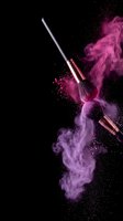 Makeup brushes with pink powder explosion on black background for cosmetic advertising and beauty product promotion.