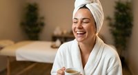 Young woman in white bathrobe and towel enjoying hot beverage at luxury spa resort. Relaxation wellness beauty treatment self-care lifestyle concept.