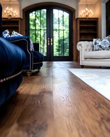 Luxurious living room interior with dark hardwood flooring, navy velvet sofa, white tufted couch, and arched French doors leading to garden view. Elegant design combines classic and modern.