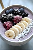 Fresh smoothie bowl with frozen berries, sliced banana and coconut flakes on light purple yogurt base, healthy breakfast concept for food blogs.