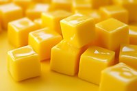 Yellow butter cubes arranged in geometric pattern on matching yellow background, showing glossy texture and soft shadows for food photography and design.