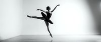 Professional ballet dancer performing grand jete leap in studio. Graceful athletic movement captured in monochrome for dance and performing arts projects.