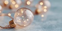 Transparent glass Christmas ornament ball with warm LED lights inside on snowy surface with bokeh background for holiday decorations and festive designs.