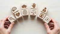 Hands arranging wooden blocks with mental health and psychology icons in circular pattern on light background for wellness concept design.