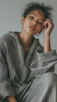 Young mixed-race woman in cozy gray hoodie with curly hair and hoop earrings posing thoughtfully against neutral background for lifestyle content.