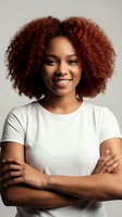 Confident young African American woman with curly red hair smiling with arms crossed wearing white t-shirt on neutral background for business portraits.