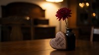 Purple chrysanthemum flower in dark vase with wooden heart decoration on table with warm bokeh lights creating cozy romantic atmosphere for home decor.