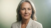 Confident mature Caucasian businesswoman with gray hair smiling in professional beige blazer against soft blurred background for corporate headshot.