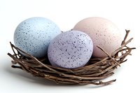 Speckled pastel Easter eggs in blue, purple, and pink resting in natural brown twig nest against white background, isolated seasonal spring holiday decoration.