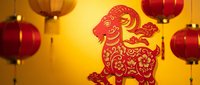 Traditional red paper cut goat zodiac symbol with ornate floral patterns surrounded by hanging Chinese lanterns on golden background for lunar new year celebrations.