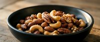 Mixed nuts assortment with cashews, almonds, walnuts and pecans in dark bowl on wooden surface for healthy snacking and cooking ingredients.