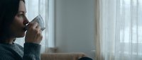 Young woman drinking hot beverage from white mug by window in cozy living room. Morning coffee ritual, relaxation and comfort at home lifestyle concept.