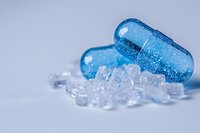 Blue transparent capsules with glitter effect next to scattered crystal fragments on light background, macro pharmaceutical photography for medical designs.