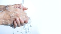 Fresh clean water flowing over cupped hands with splashing droplets against white background for hygiene and wellness concepts.
