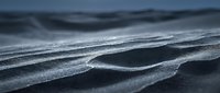 Close-up of rippled sand surface with water droplets and wave patterns, suitable for backgrounds, textures, nature projects, and environmental design work.