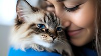 Young Caucasian woman with blonde hair embracing fluffy Ragdoll cat with blue eyes, showing tender connection between pet owner and feline companion.