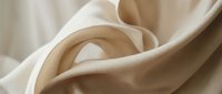 Soft beige silk fabric with elegant folds and curves creating luxurious textile waves for fashion design and interior decoration projects.