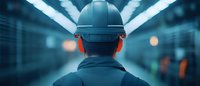 Construction worker wearing protective helmet viewed from behind in industrial environment with blue lighting and bokeh effect creating futuristic atmosphere.