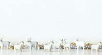 Herd of decorative reindeer and deer figurines in white, gray, and gold tones arranged in a row on neutral background for holiday and seasonal design projects.
