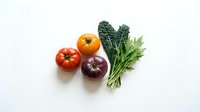 Fresh organic vegetables including ripe tomatoes, leafy kale, purple onion and herbs arranged on clean white background for healthy cooking concepts.