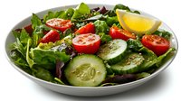 Fresh garden salad with sliced cucumber, cherry tomatoes, mixed greens and lemon wedge garnish on white ceramic plate against dark background.