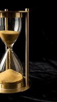 Golden sand flows through glass chambers of brass hourglass against dark background, symbolizing passage of time, deadline urgency, and temporal measurement for business and productivity concepts.