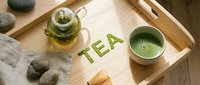 Matcha green tea set on wooden tray with word TEA made from powder, glass teapot, whisk, and stones for zen wellness concept.