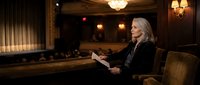 Mature blonde businesswoman reading documents in elegant hotel lobby with warm lighting and luxury furniture for corporate hospitality concepts.