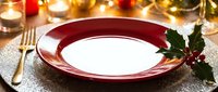 Elegant red plate with holly garnish on glittering gold tablecloth, surrounded by candles and gold cutlery, ready for festive holiday dining and celebration table settings.