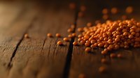 Raw red lentils scattered on rustic wooden table surface with dramatic lighting and shallow depth of field, creating moody food photography atmosphere.