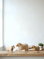 Wooden sheep figurines arranged on natural wood shelf against white wall with minimalist decor and small potted plant for home interior styling.