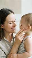 Loving mother gently touching baby's face in tender moment of bonding and affection at home showing maternal care and family connection.