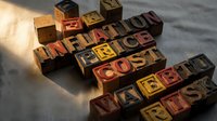 Wooden letter blocks spelling inflation, price, cost, wages, and crisis on dark surface with dramatic lighting for economic concepts.