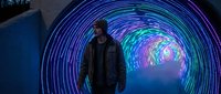 Young man walking through futuristic neon tunnel with colorful LED lights creating circular patterns in modern urban environment for technology concepts.