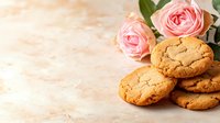 Fresh baked homemade cookies with crackled surface and pink garden roses on light textured background with copy space for bakery design.